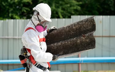 Workers wearing protective clothing while removing the asbestos roof. Hazardous waste management and working safety concept. Professional waste disposal.
