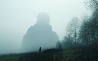A double exposure of an atmospheric half transparent man looking at a person standing on the edge of a forest in the countryside. On a moody foggy winters day.       