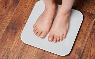 Woman feet on white scale in wooden floor background