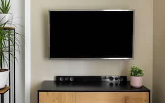 smart tv mockup hanging on beige wall in modern interior with green plants. blank screen