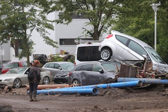 epa09347912 A person stands in front of damaged cars after flooding in Bad Neuenahr-Ahrweiler, Germany, 16 July 2021. Large parts of Western Germany were hit by heavy, continuous rain in the night to 15 July resulting in local flash floods that destroyed buildings and swept away cars.  EPA/FRIEDEMANN VOGEL