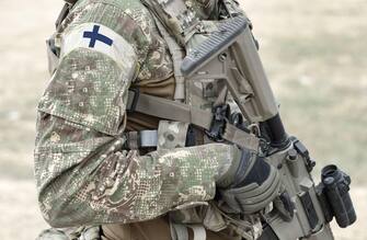Soldier with assault rifle and flag of Finland on military uniform. Collage.
