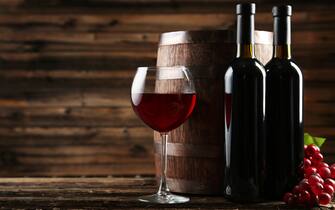 Red wine glass with bottle and barrel on brown wooden background