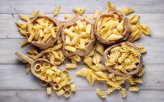 Assortment of raw pasta: pens, shells, rigatoni, fusilli and squid on wooden background, top view.