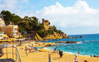 Lloret de Mar, Catalonia, Spain, 02 October 2019. Tourists on the beach of Lloret de Mar below the Castell de Plaja, a castle-like house from the 1940s. Costa Brava.