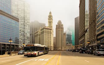 Misty fog  makes wits way into the city of Chicago, enveloping the tops of several buildings. The beautiful and historic Wrigley Building and Tribune Tower stand in the center of the composition which was created looking down the center of on of the city streets.