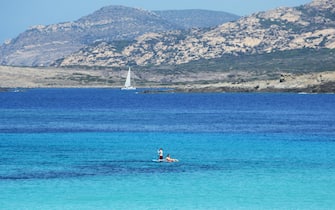 Scenic view of the Asinara island coastline on a summer day with a white sailboat in the beautiful turquoise Mediterranean sea