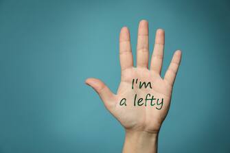 Left-handed woman holding open palm on light blue background, closeup