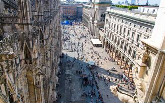 Crowd of small figures of many people are walking on Piazza del Duomo square near Gallery Vittorio Emanuele II in historical city centre, top view fro