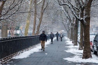 epa11090537 People walk along the edge of Tompkins Square Park as snow falls in New York, New York, USA, 19 January 2024.  EPA/SARAH YENESEL