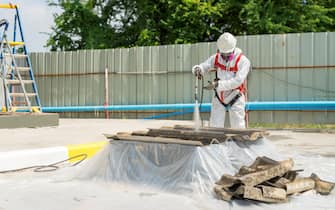 Worker wearing full body protective clothing while working with the asbestos roof. Hazardous waste management and working safety concept. Professional waste disposal.