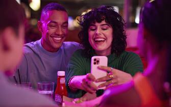 Cheerful woman taking selfie with man on smart phone by friends at bowling alley
