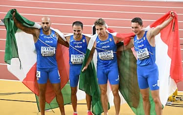 (L to R) Italy's Lamont Marcell Jacobs, Lorenzo Patta, Roberto Rigali, and Filippo Tortu pose with their national flags after the men's 4x100m relay final during the World Athletics Championships at the National Athletics Centre in Budapest on August 26, 2023. (Photo by Attila KISBENEDEK / AFP) (Photo by ATTILA KISBENEDEK/AFP via Getty Images)