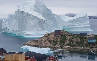 A picture taken on July 13, 2018 shows an iceberg behind houses and buildings after it grounded outside the village of Innarsuit, an island settlement in the Avannaata municipality in northwestern Greenland. (Photo by MAGNUS KRISTENSEN / Ritzau Scanpix / AFP) / Denmark OUT (Photo by MAGNUS KRISTENSEN/Ritzau Scanpix/AFP via Getty Images)