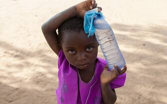 A 5-year old girl, wearing a purple dress, carries a plastic bottle of water, in a small village in the southern district of Nsanje, Malawi, during the drought of 2016.