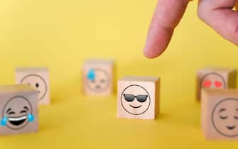 The finger points to a smiley emoji with glasses on a yellow background. The concept of the world day of emoticons.