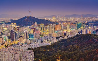 High angle view of Namsan Seoul Tower surrounded by cityscape of Seoul illuminated with lights in the twilight view from Inwang mountain. Seoul, South Korea