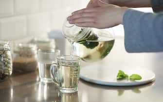 Woman pouring fresh mint tea into a glass from a glass teapot, close up.
