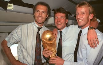FILED - 09 July 1990, Italy, Rom: On the plane returning from Rome to Frankfurt, former DFB team manager Franz Beckenbauer (l), captain and midfielder Lothar Matthäus (M) and defender Andreas Brehme, who scored the decisive goal, present the World Cup trophy. Franz Beckenbauer is dead. The German soccer legend died on Sunday at the age of 78, his family told the German Press Agency on Monday. Photo: Wolfgang Eilmes/dpa (Photo by Wolfgang Eilmes/picture alliance via Getty Images)