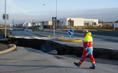 This photo taken on November 13, 2023 shows a member of the emergency services walking near a crack cutting across the main road in Grindavik, southwestern Iceland following earthquakes. The southwestern town of Grindavik -- home to around 4,000 people -- was evacuated in the early hours of November 11 after magma shifting under the Earth's crust caused hundreds of earthquakes in what experts warned could be a precursor to a volcanic eruption.  The seismic activity damaged roads and buildings in the town situated 40 kilometres (25 miles) southwest of the capital Reykjavik, an AFP journalist saw. (Photo by Kjartan TORBJOERNSSON / AFP) / Iceland OUT (Photo by KJARTAN TORBJOERNSSON/AFP via Getty Images)