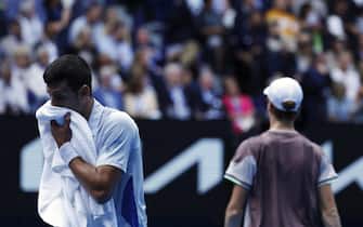 epa11104772 Novak Djokovic (L) of Serbia wipes his face with a towel as Jannik Sinner of Italy walks past during the Men's semi final match at the Australian Open tennis tournament in Melbourne, Australia, 26 January 2024.  EPA/MAST IRHAM