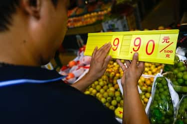 A fruit and vegetable vendor updates the price of an item at a market in Beijing on August 9, 2023. (Photo by Pedro PARDO / AFP) (Photo by PEDRO PARDO/AFP via Getty Images)
