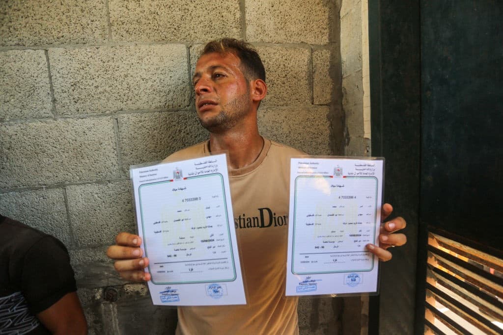 DEIR AL BALAH, GAZA - AUGUST 13: Palestinian father Mohammed Abu al-Qumsan, who was forced to flee from the northern Gaza Strip to Deir Al Balah city due to Israeli attacks, cries and mourns as he shows the birth certificates of his twins after he learnt the news that his wife, 4-day-old twins babies and mother had died following Israeli attacks at the morgue of Al-Aqsa Martyrs Hospital in Deir Al Balah, Gaza on August 13, 2024. Palestinian father al-Qumsan went to issue a birth certificate for his twin babies born four days ago then he received the news that his family was injured in the Israeli attacks while he was bringing home the birth certificate he had issued, and when he arrived at Al-Aqsa Martyrs Hospital in the city, he learned that he lost his entire family. (Photo by Ashraf Amra/Anadolu via Getty Images)