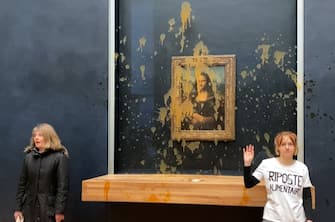 This image grab taken from AFPTV footage shows two environmental activists from the collective dubbed "Riposte Alimentaire" (Food Retaliation) gesturing as they stand in front of Leonardo Da Vinci's "Mona Lisa" (La Joconde) painting after hurling soup at the artwork, at the Louvre museum in Paris, on January 28, 2024. Two protesters on January 38, 2024 hurled soup at the bullet-proof glass protecting Leonardo da Vinci's "Mona Lisa" in Paris, demanding the right to "healthy and sustainable food", an AFP journalist said. It is the latest attack on the masterpiece in the French capital's Louvre museum, after someone threw a custard pie at it in May 2022, but it's thick glass casing ensured it came to no harm. (Photo by David CANTINIAUX / AFPTV / AFP) (Photo by DAVID CANTINIAUX/AFPTV/AFP via Getty Images)
