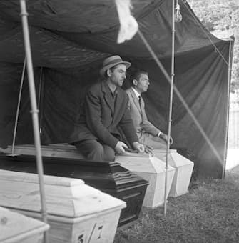 Under a tent, a pair of survivors sit astride coffins, Longarone, near the Vajont Dam in the Piave Valley, Italy, early October, 1963. On October 9, a landslide in the dam basin caused a wave more than 800 feet high to overtop the dam and flood the valley below--five villages were completely destroyed, more than 2000 people were killed, and thousands more were left homeless and displaced. (Photo by Archivio Cameraphoto Epoche/Getty Images)