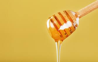 Honey flows down from a honey bucket on a yellow background. The concept of healthy and eco-friendly nutrition