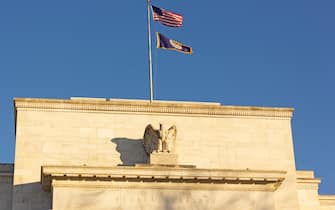 United States Federal Reserve headquarters in Washington DC, USA. Eccles Building with US National and Fed flags under clear sky in early morning.