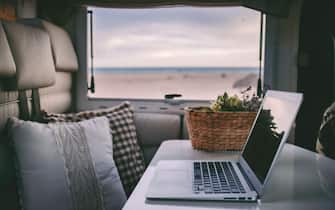 Laptop computer in a camper on the beach, concept - vacation, flexibility, freedom, smart working, independence, digital nomads