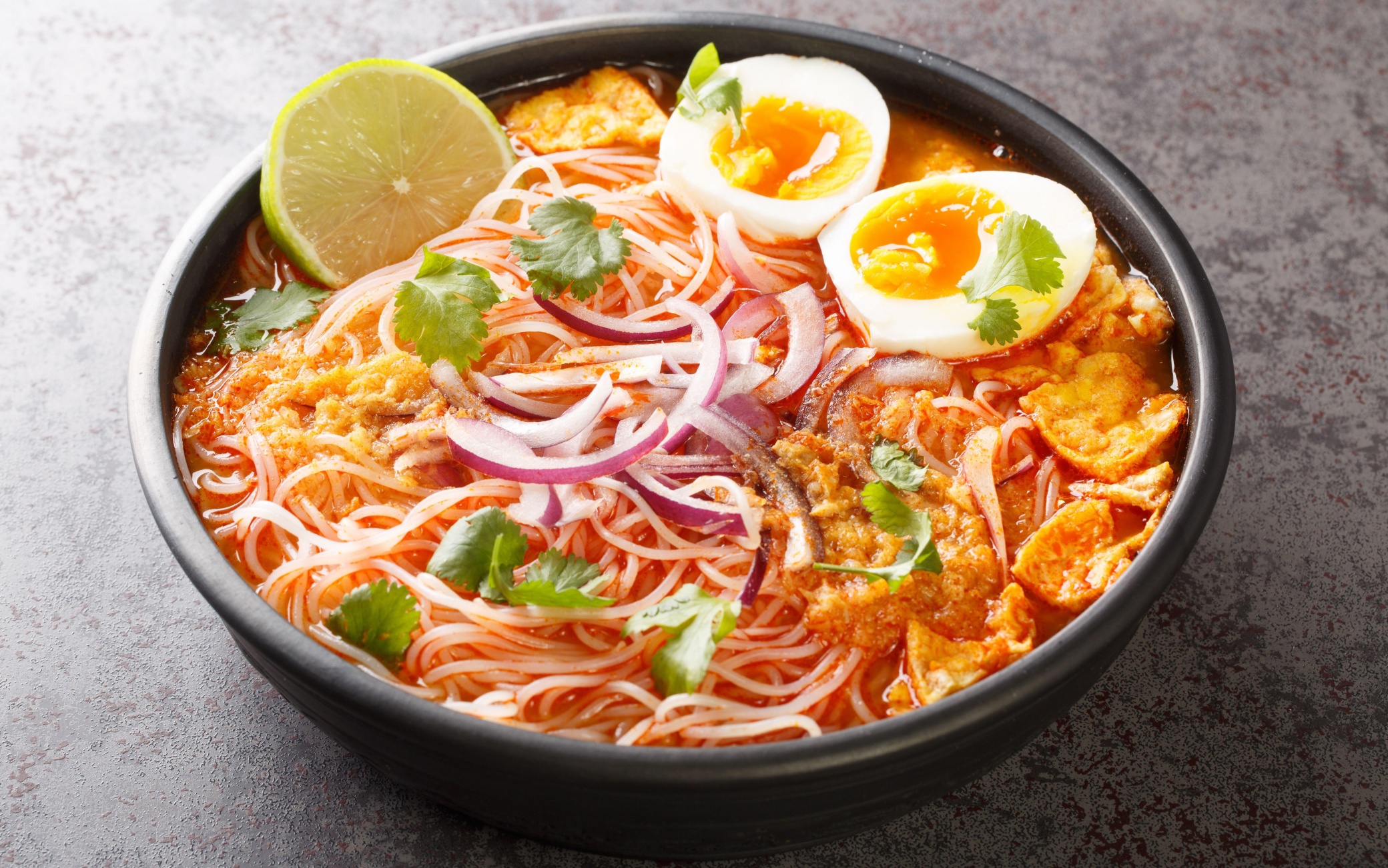 Burmese Mohinga Rice Noodle Fish Soup closeup in the bowl on the table. Horizontal