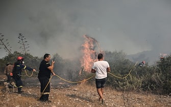 Firefighters and a civilian try to extinguish wildfires near the village of Vati, just north of the coastal town of Gennadi, in the southern part of the Greek island of Rhodes on July 25, 2023. Some 30,000 people fled the flames on Rhodes at the weekend, the country's largest-ever wildfire evacuation as the prime minister warned that the heat-battered nation was "at war" with several wildfires and spoke of three difficult days ahead.. (Photo by Spyros BAKALIS / AFP) (Photo by SPYROS BAKALIS/AFP via Getty Images)