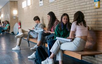 Some high school students sitting on a bench in the hallway, chatting with each other while in between lessons.
