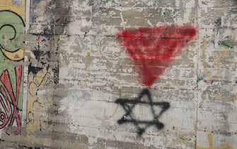 A Palestinian woman walks past a graffiti of the Star of David under an inverted “red triangle”, a symbol that the Palestinian Hamas movement's military wing Al-Qassam Brigades uses to identify Israeli targets in their videos, in the occupied West Bank city of Hebron on November 30, 2023, on the seventh day of a truce between Israel and Hamas. The warring parties have agreed a pause in fighting to allow time for the militant group to release Israeli hostages in exchange for Palestinian prisoners. (Photo by HAZEM BADER / AFP)