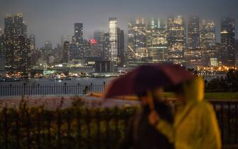 WEEHAWKEN, NEW JERSEY - SEPTEMBER 29: People walk under rain while the New York skyline is covered with clouds during a coastal storm on September 29, 2023 as seen from Weehawken, New Jersey. Flash flooding is expected in the counties of Nassau, Queens and Kings, which includes Brooklyn, according to the state's National Weather Service office as remnants of Tropical Storm Ophelia reaches the Northeast. Gov. Kathy Hochul has declared a state of emergency for the NYC area.  (Photo by Eduardo Munoz Alvarez/Getty Images)