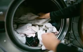 Young caucasian woman hands putting her dirty clothes in the washing machine in a laundromat. Self service laundry