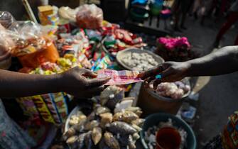 A customer pays with a Ghana cedi banknote at a food market in Accra, Republic of Ghana, on Wednesday, Nov. 3, 2021. Ghana’s inflation rate breached the central bank’s target band in September after supply bottlenecks, a weak cedi and surging energy costs propelled food-price growth to a seven-month high. Photographer: Nipah Denis/Bloomberg