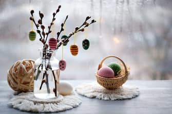 Easter decorations on windowsill in Spring. Wooden painted eggs on pussy willow twigs in glass bottle, Easter eggs in basket, rustic ball, macrame