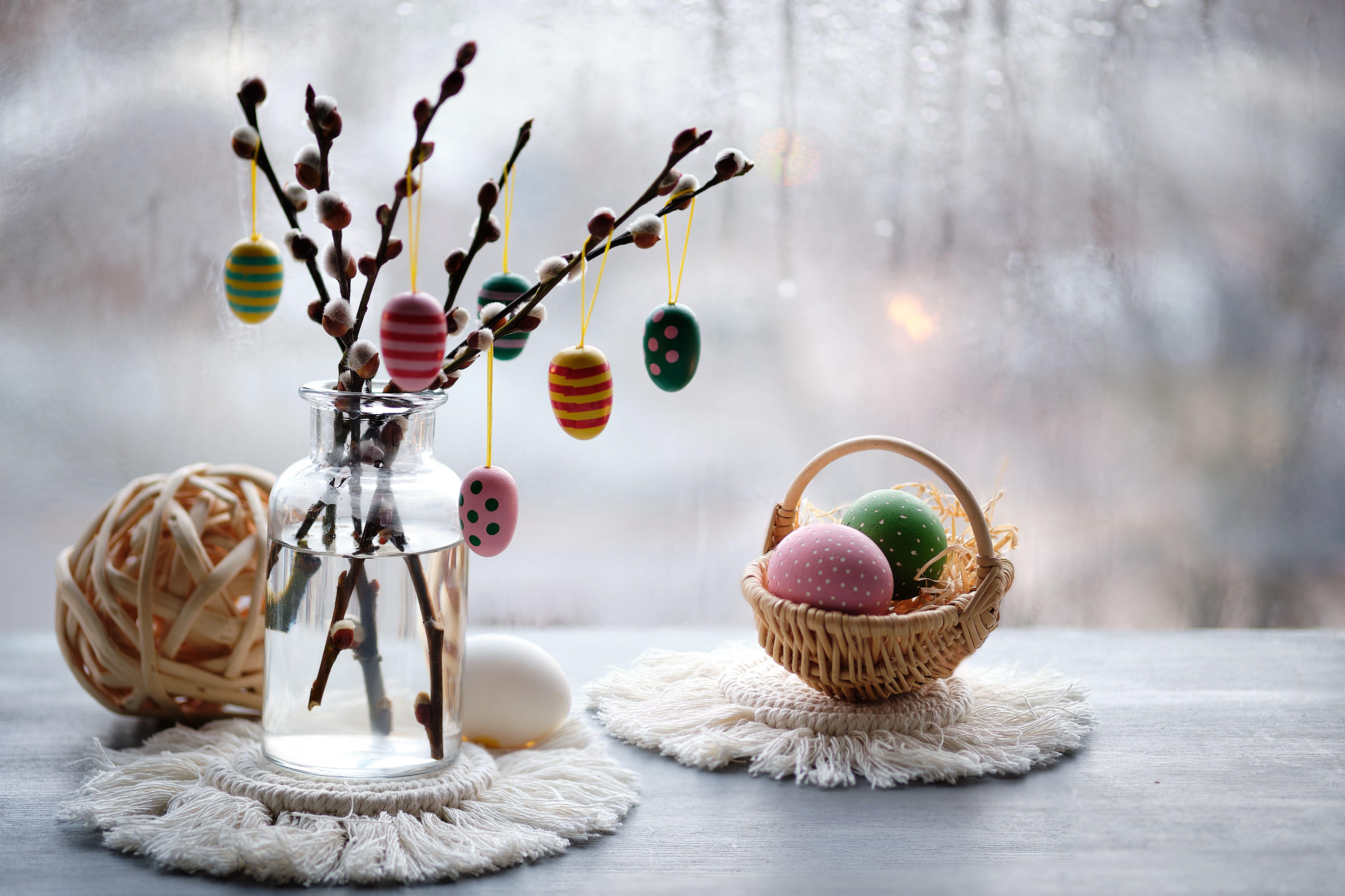 Easter decorations on windowsill in Spring. Wooden painted eggs on pussy willow twigs in glass bottle, Easter eggs in basket, rustic ball, macrame