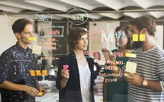 Business people discussing over plan on glass wall in office