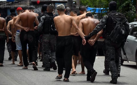 Police officers escort suspects arrested during the Operacao Contencao (Operation Containment) out of the Vila Cruzeiro favela, in the Penha complex, in Rio de Janeiro, Brazil, on October 28, 2025. At least 2,500 agents took part in an operation to arrest drug traffickers from the Comando Vermelho (CV), which resulted in, at least, 18 suspects and several police officers dead. (Photo by Mauro PIMENTEL / AFP)