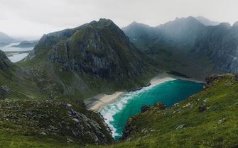 Scenic landscape of the turquoise-colored beach surrounded by the green mountain peaks, view from Ryten mountain on Lofoten, Nordland, Northern Norway