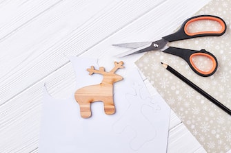 Cut out wooden deer, scissors, pencil. Draw template of deer on paper, pencil, scissors, wooden silhouette of deer animal on wooden background, top view.