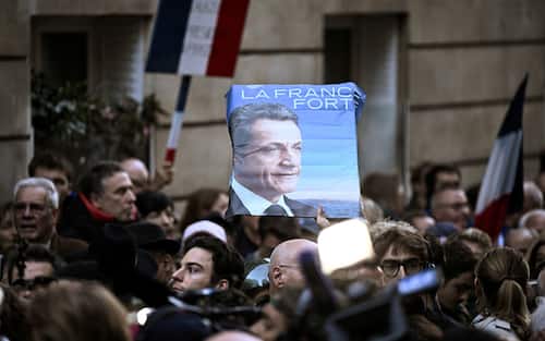 Supporters of France's former president Nicolas Sarkozy gather outside his residence ahead of his departure to La Sante prison for incarceration on a five-year prison sentence, after being convicted of criminal conspiracy over a plan for late Libyan dictator Moamer Kadhafi to fund his 2007 electoral campaign, in Paris, on October 21, 2025. Nicolas Sarkozy, who has faced a flurry of legal woes since losing re-election in 2012, is to be jailed on October 21, 2025, over a scheme to acquire Libyan funding for his successful 2007 presidential run, becoming the first former head of a European Union country to serve time behind bars. The former French right-wing leader has appealed the verdict and denounced an "injustice". (Photo by JULIEN DE ROSA / AFP)