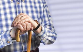 Close up of a pensioner resting his hands on a walking stick