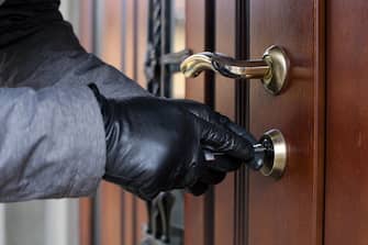 a thief in gloves opens the door lock of a private house and penetrates inside in broad daylight