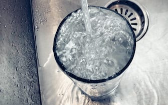 Tap water filling and spilling out of a large glass in a stainless steel sink
