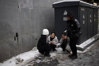 epa11030664 Women smoke cigarettes protecting themselves from wind in a street of Beijing, China, 14 December 2023. Beijing Meteorological Observatory has issued a Cold Wave alert for 15 and 16 December.  EPA/ANDRES MARTINEZ CASARES